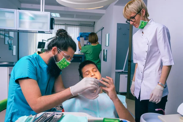 歯医者と助手は１０代の少年患者の歯を調べる — ストック写真