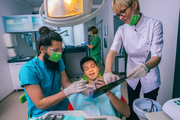 男性歯科医と女性アシスタントショー若い男の子患者彼の歯X線画像で歯科事務所 — ストック写真