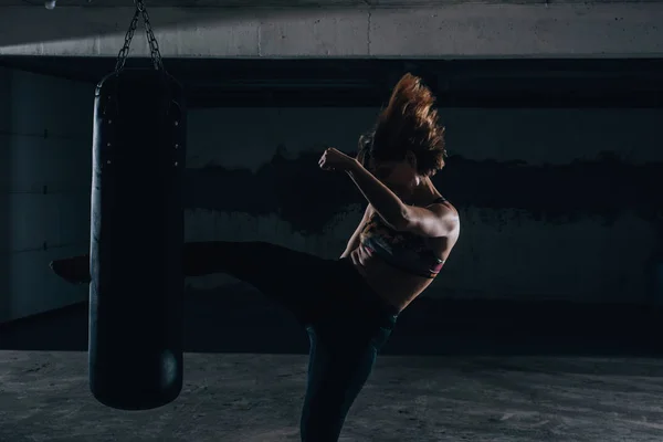 Молодая Силуэт Женщина Практикует Высокий Удар Боксерской Сумкой Внутри Гаража — стоковое фото