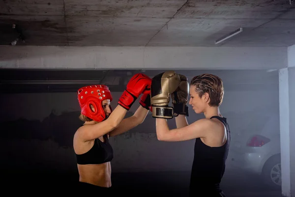 Two female boxers putting on boxing gloves before their fight inside a garage