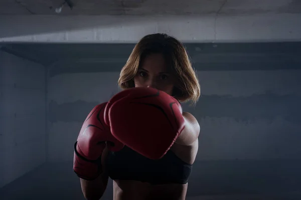 年轻迷人的健身女子在车库里用红色拳击手套练拳的肖像 — 图库照片