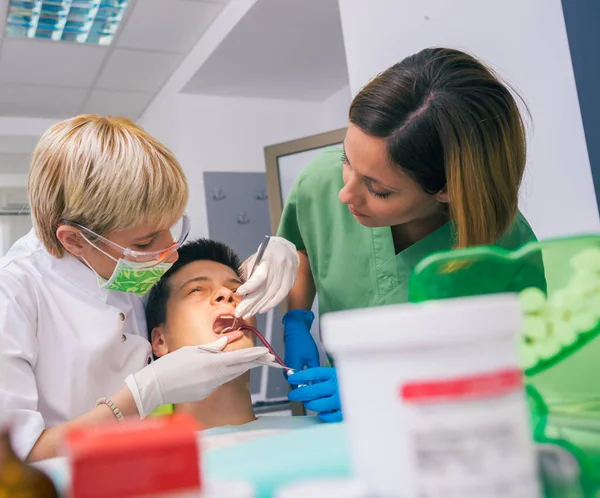 彼女の助手の助けを借りて歯医者は十代の男の子の患者の口と歯を調べます — ストック写真