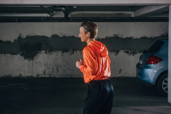 一名身穿橙色帽衫的女运动员在车库里准备运动的画像 — 图库照片