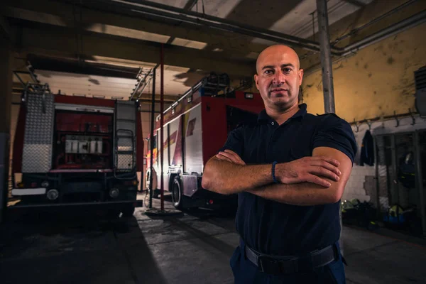 Portrét pohledného hasiče stojícího proti hasičským vozům — Stock fotografie