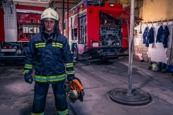 Um bombeiro com uniforme e capacete segurando uma motosserra com fogo t — Fotografia de Stock