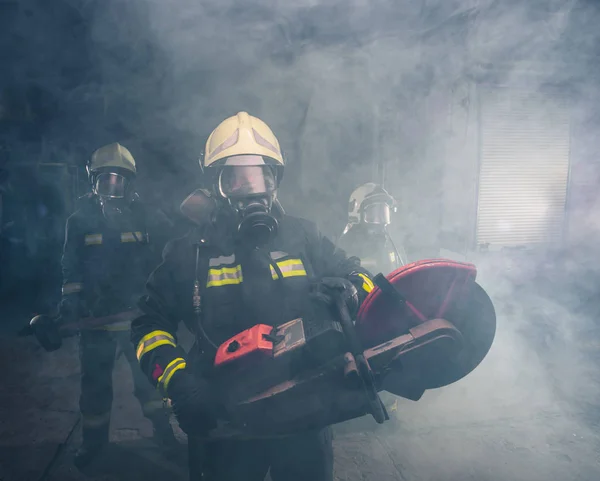 Ritratto di vigile del fuoco che tiene una motosega di salvataggio nel garage fumoso di — Foto Stock