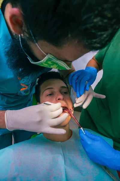 Male dentist with the help of a female dentist examines the mouth and teeth of a teenage boy patient.