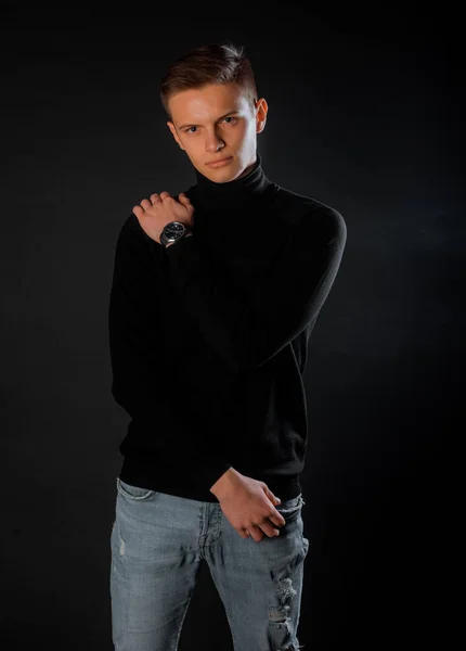 ブルーデニムパンツを着たハンサムな若い男の肖像画 黒の背景に隔離された黒プルオーバー — ストック写真