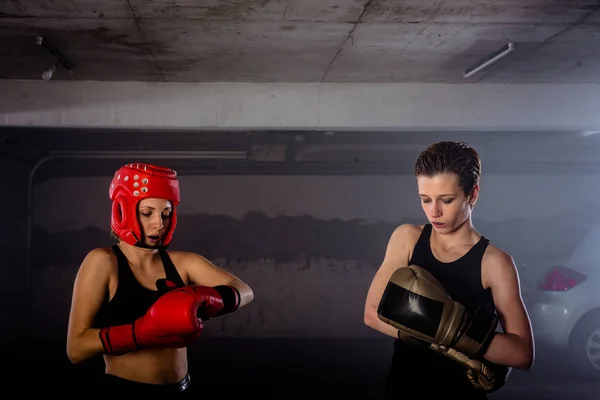 Two female boxers putting on boxing gloves before their fight inside a garage