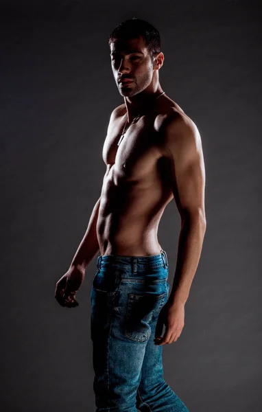 スタイリッシュな若い男身に着けている青デニムパンツポーズ半分裸 — ストック写真