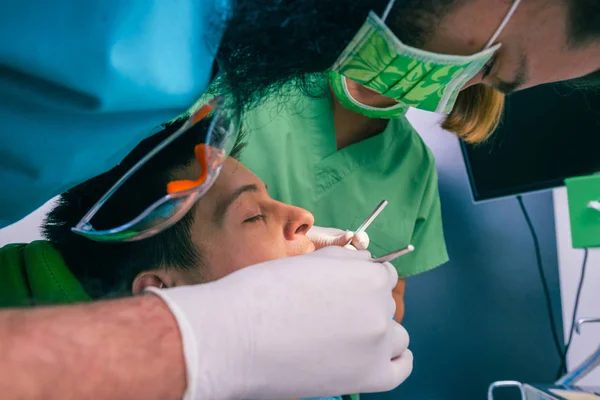 Male dentist with the help of a female dentist examines the mouth and teeth of a teenage boy patient.