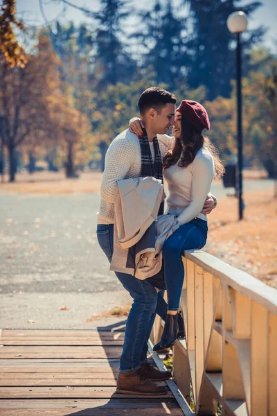 Graceful couple wearing jeans and white blouses is kissing in the park on a autumn day