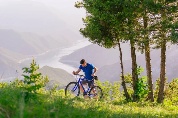 身穿蓝色衬衫的山地骑车人一边骑着自行车穿过绿林 一边欣赏那迷人的风景 — 图库照片