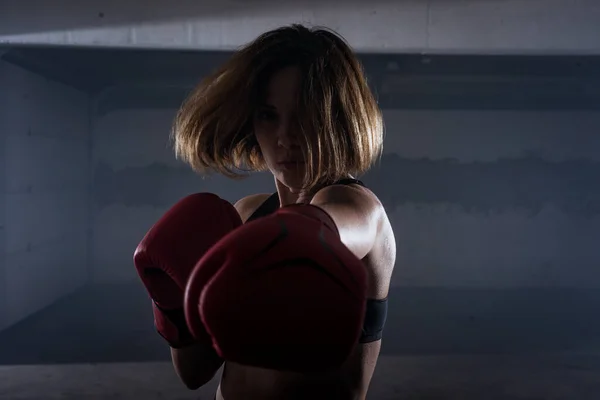 年轻迷人的健身女子在车库里用红色拳击手套练拳的肖像 — 图库照片