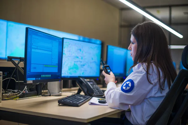 Female security guard sitting and monitoring modern CCTV cameras in a surveillance room.