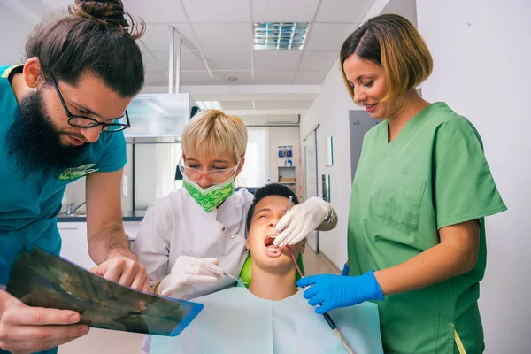 若い男の子の歯が検査されている間に彼の女性の同僚にX線写真を説明ひげを生やした歯科医 — ストック写真