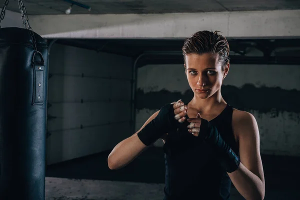 写真の焦点を当てた若い女性準備彼女の黒包帯のためにボクシングのためにガレージ — ストック写真