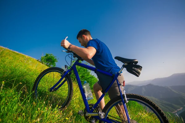 一个健康的山地骑车人把他的自行车推上了山坡 背景是森林 河流和山脉 景色令人叹为观止 日落时令人惊奇的绿色天性 — 图库照片
