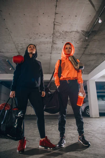 Two female boxer friends standing in a garage with boxing equipment