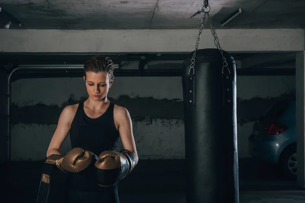 Strong woman with short hair putting on her gold boxing gloves