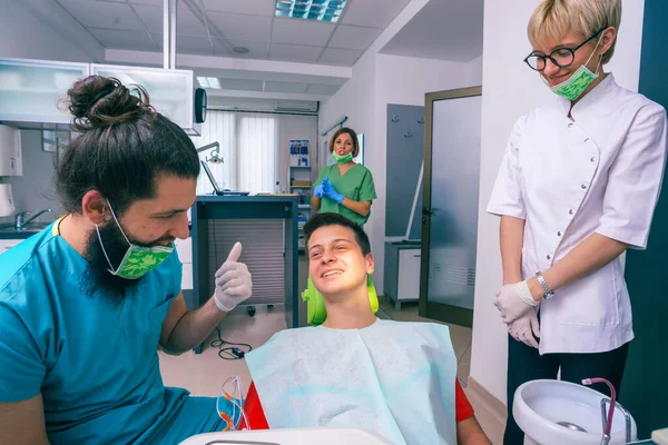 幸せな十代の患者は彼らが彼に歯科治療を説明している間彼の歯科医に笑みを浮かべている — ストック写真