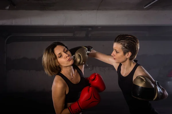 Close-up image of two female boxers with protective equipment exercising punching and boxing