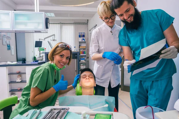 10代の男の子の患者にX線写真を示す男性歯科医の肖像画一方 彼の笑顔の女性の同僚は彼を助けている — ストック写真