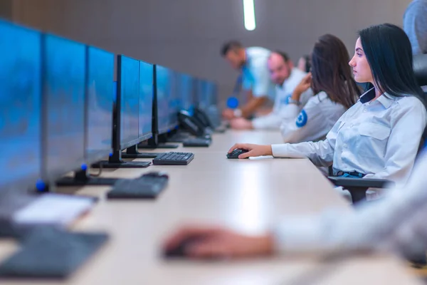 Group of Security data center operators (administrators) working in a group at a CCTV monitoring room while looking at multiple monitors ( computer screens)