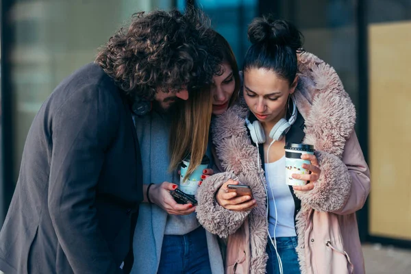 三个朋友一边站在一起一边看着电话 一边举着一杯咖啡 — 图库照片