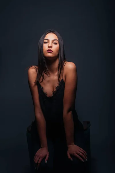 漂亮的女模特 穿着性感的黑色背心和黑色裤子 在摄影棚里的椅子前摆姿势 — 图库照片