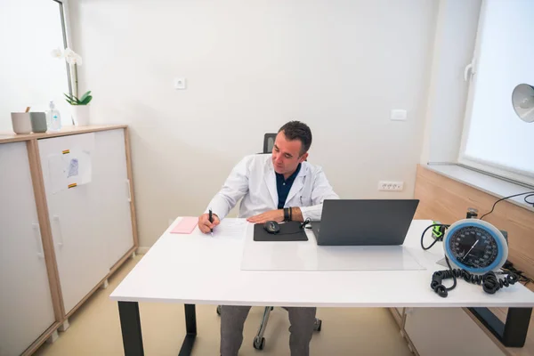 Médico Meia Idade Sentado Seu Escritório Escrevendo Prescrições — Fotografia de Stock