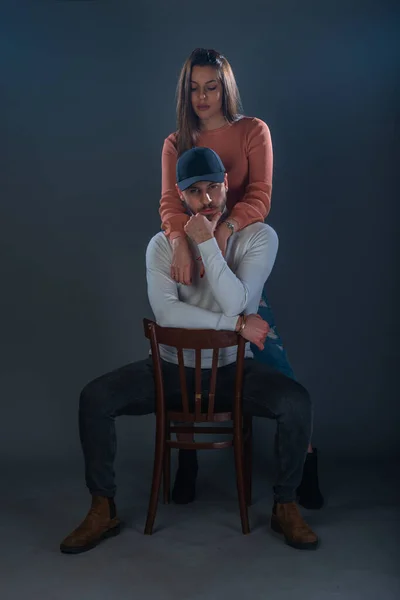 一个英俊的男人坐在椅子上 一个美丽的女人站在他旁边 背景漆黑 在工作室里 — 图库照片