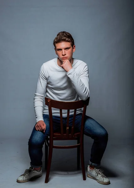 椅子に座っているモダンなスタイルの服を着て流行の若い男のスタジオボディショット — ストック写真