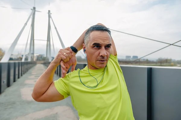 Older well built man in activewear stretching out his body before running