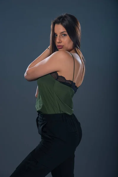 スタジオに立つセクシー若い女性モデルの肖像と身に着けていますダークグリーンの上と黒のパンツ — ストック写真