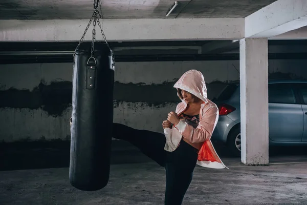 年轻的女运动员在车库里练拳击时踢得很高 — 图库照片