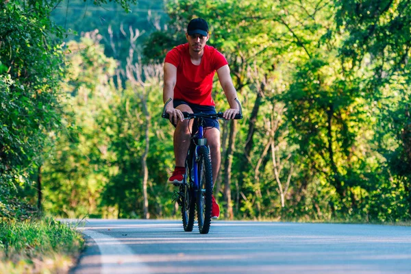 骑自行车的人 戴着棒球帽和红色T恤 骑自行车在一条空旷的路上 — 图库照片
