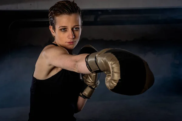 Closeup picture of beautiful female boxer practicing her punches with gold boxing gloves