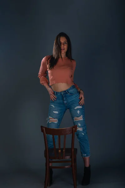 Kobieta Modelka Pomarańczowej Bluzce Dżinsach Pozujących Przed Drewnianym Krzesłem — Zdjęcie stockowe