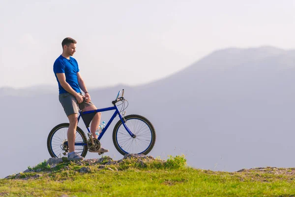 适合骑自行车的山地骑手骑着自行车在山顶上的青草地上行驶 — 图库照片