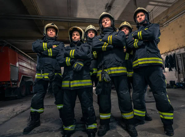 武装して自信を持って立って消防士のグループが交差した 救急車の準備ができて消防士 — ストック写真
