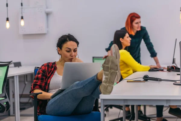 年轻女人坐在办公室的桌子旁 双腿放在桌子上 同时在笔记本电脑上工作 — 图库照片