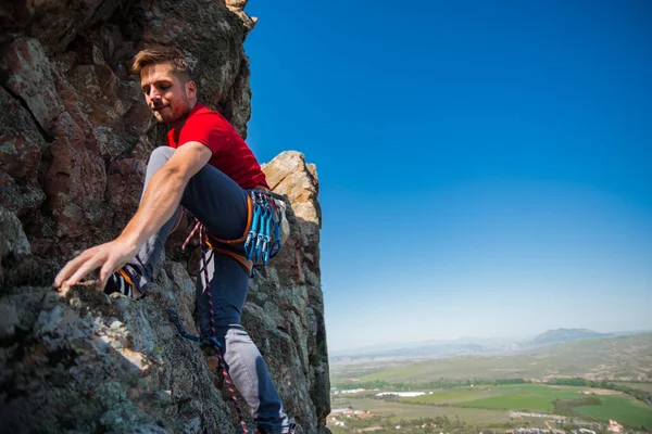 若い男は日の出に山のある谷の岩壁に登る — ストック写真