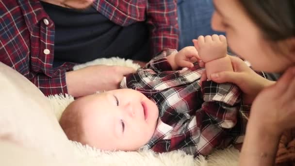 Молодая красивая семья лежит в постели и целует ребенка — стоковое видео