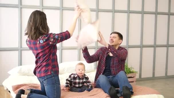 Egy boldog család van bolondozás körül az ágyban, anya és apa harcolnak a párnák, a fia mellettük — Stock videók