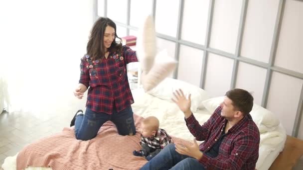 Una familia feliz está jugando en la cama, mamá y papá están peleando con almohadas, el hijo está a su lado — Vídeos de Stock