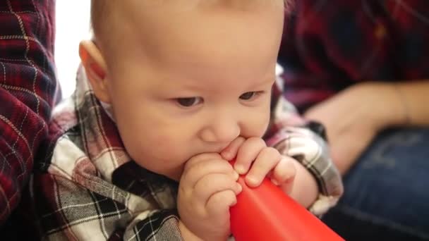 Menino pequeno feliz colocar um brinquedo em sua boca enquanto sentado — Vídeo de Stock