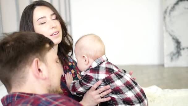 Gelukkige ouders liggen met hun schattige baby zoon op bedat thuis in slaapkamer — Stockvideo