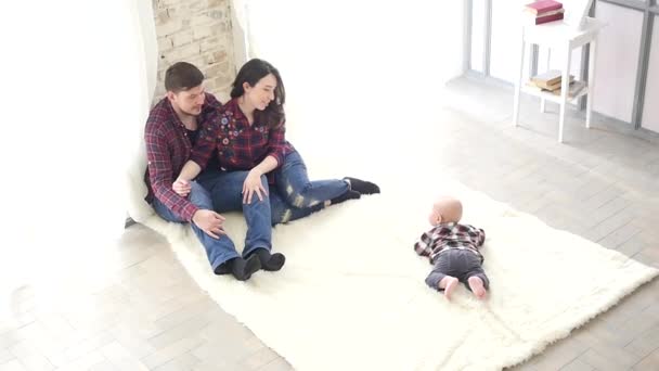 Молодая семья сидит в холле дома и смотрит на своего ребенка — стоковое видео