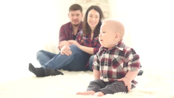 Um bebê bonito se senta no chão e olha para seus pais — Vídeo de Stock